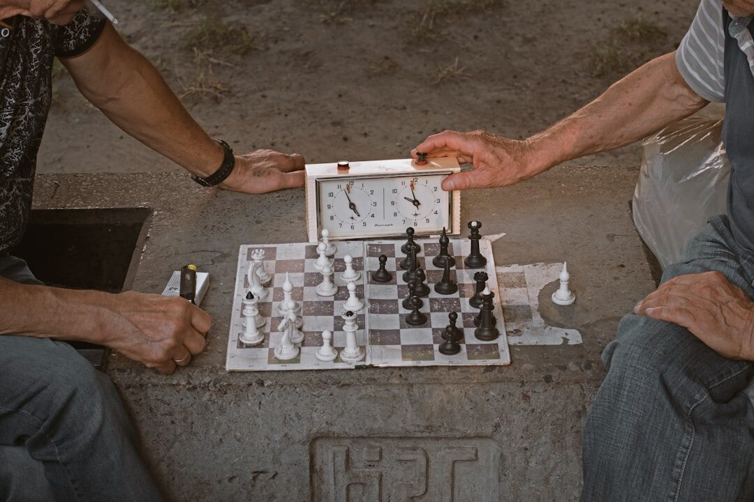 Two senior men playing chess at a small table while others watch