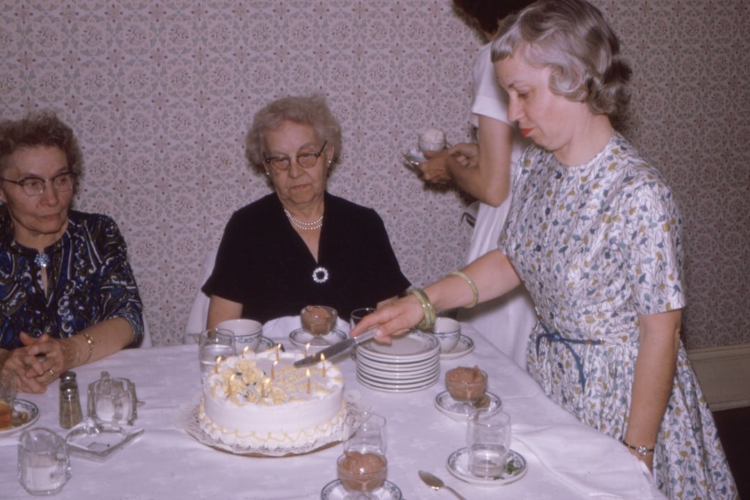 Senior woman blowing out candles on a birthday cake surrounded by friends